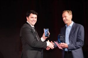 Anton Kivell accepting an award on behalf of DCSS, with Dan Crocker on video call on a smartphone.